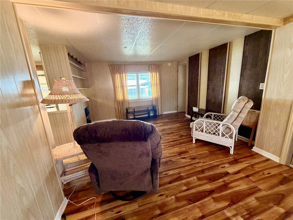 A living room features wood-look flooring, wood-paneled walls, a recliner, and a wicker chair — 6363 KILEPA COURT, NORTH PORT, FL