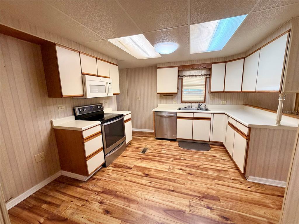 A kitchen features white cabinets, stainless steel appliances, and wood-look flooring — 6363 KILEPA COURT, NORTH PORT, FL