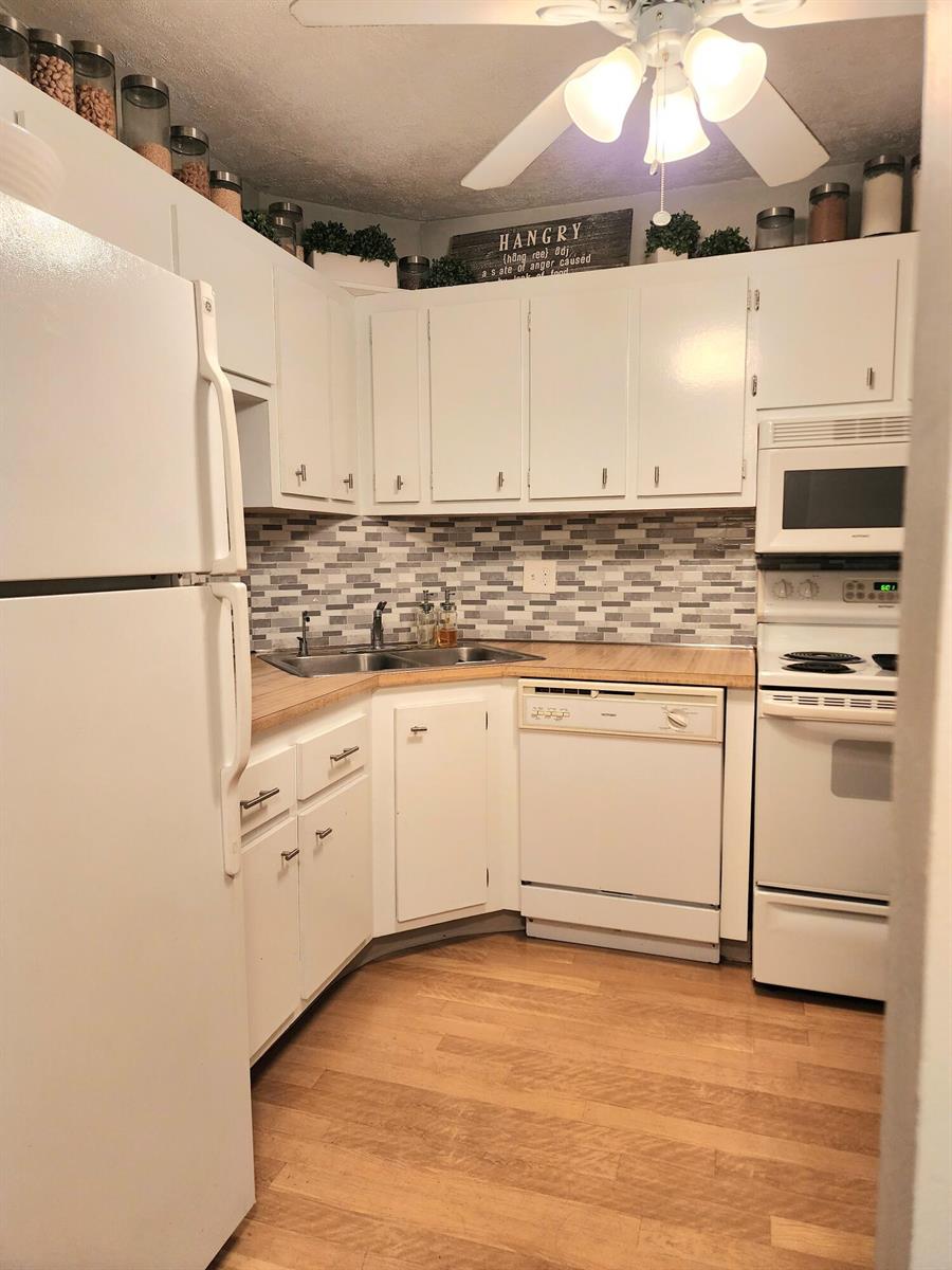 A kitchen features white cabinets, a tiled backsplash, wood countertops, and white appliances — 285 SE 10th Street # 8a, Deerfield Beach FL 33441, DEERFIELD BEACH, FL