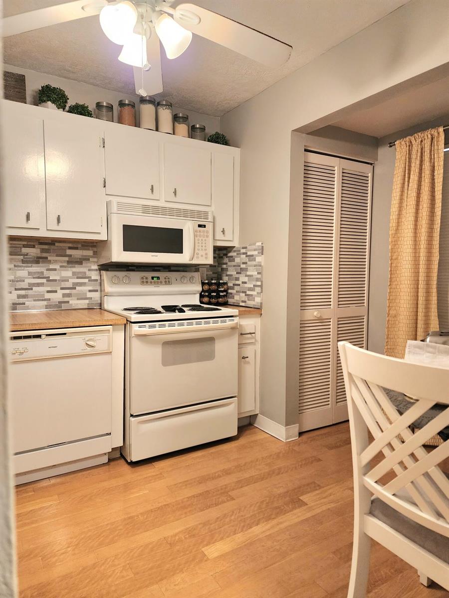 A kitchen features white cabinets, a white stove, a dishwasher, and a gray tiled backsplash — 285 SE 10th Street # 8a, Deerfield Beach FL 33441, DEERFIELD BEACH, FL