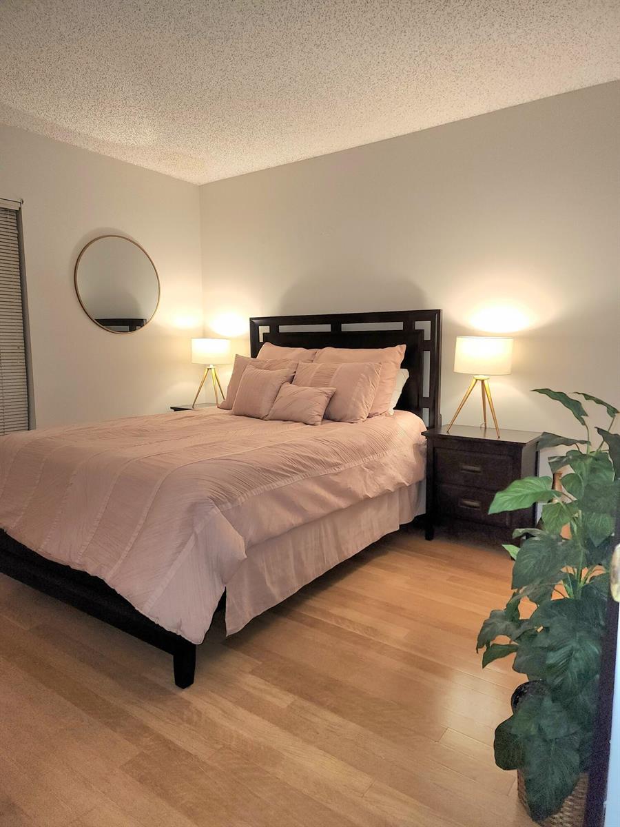 A bedroom features a dark wood bed frame, blush bedding, two bedside lamps, and wood flooring — 285 SE 10th Street # 8a, Deerfield Beach FL 33441, DEERFIELD BEACH, FL