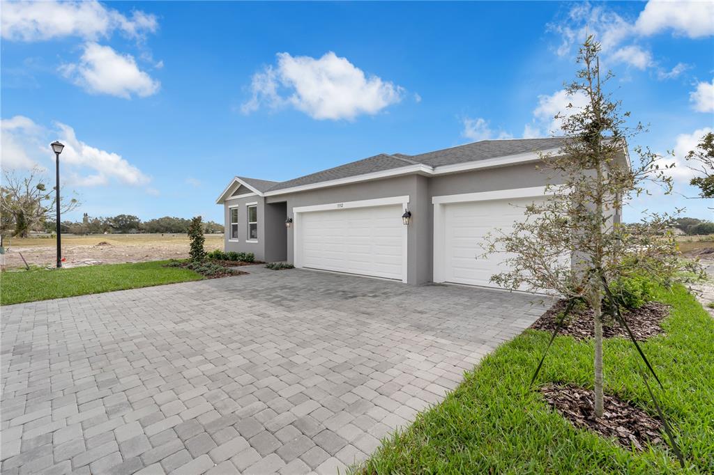 A gray house with a three-car garage and a paved driveway under a blue sky — 1012 BANFF DRIVE NE, PALM BAY, FL