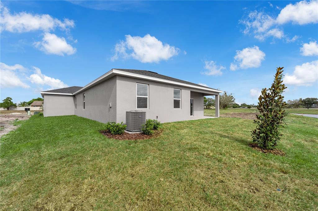 The exterior of a gray, single-story house features a covered patio and an air conditioner — 1012 BANFF DRIVE NE, PALM BAY, FL