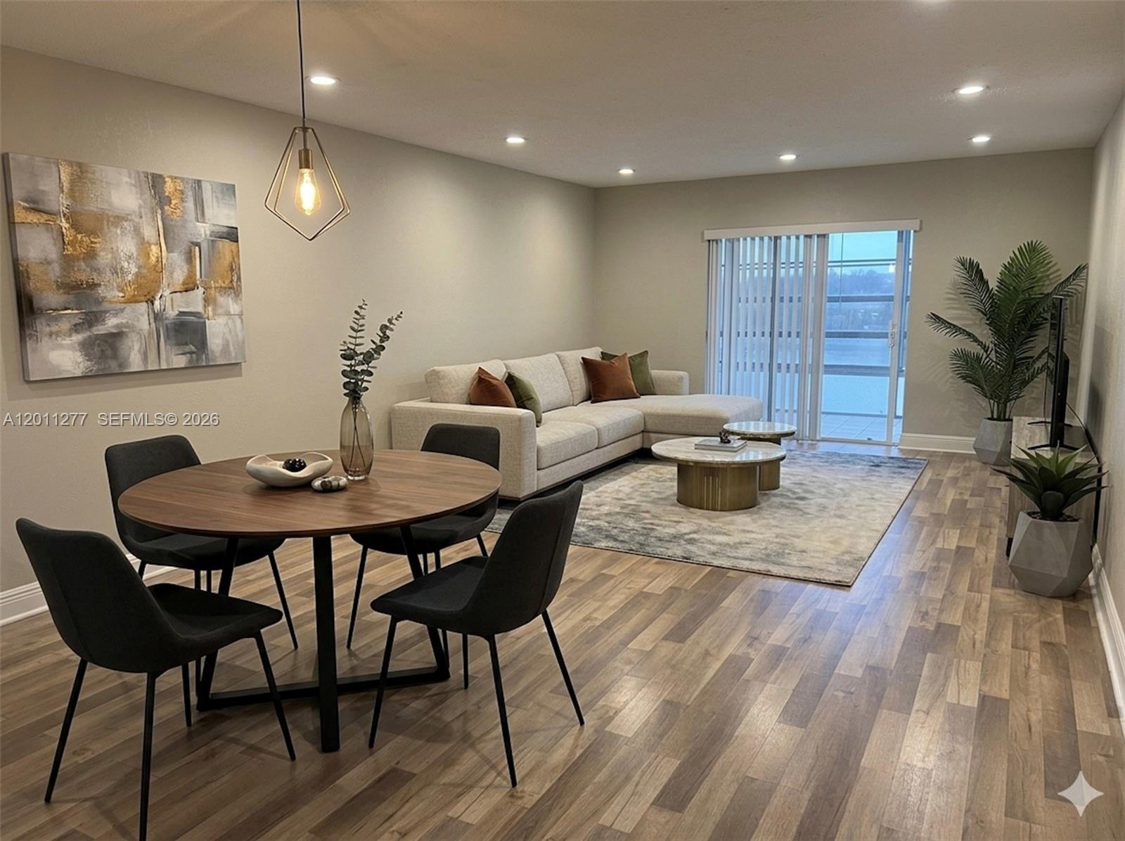 An open-concept living and dining area features wood-look flooring, a sectional sofa, and a table — 879 NE 195th St # 425, Miami FL 33179, MIAMI, FL