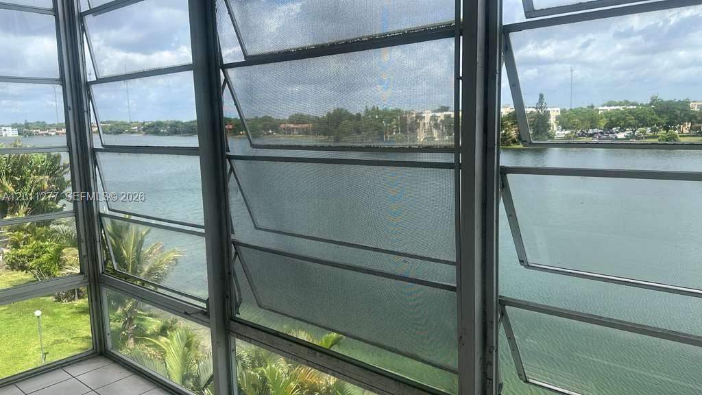 A sunroom features jalousie windows overlooking a lake and surrounding greenery — 879 NE 195th St # 425, Miami FL 33179, MIAMI, FL