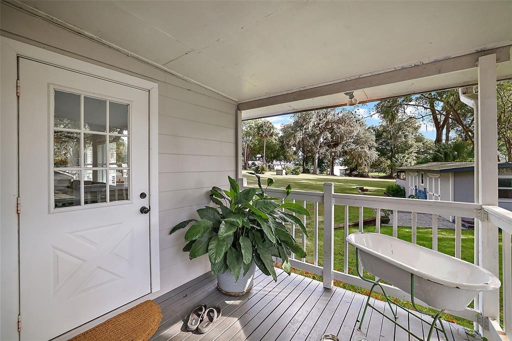 A covered wooden porch features a white door, a potted plant, and a vintage bathtub — 10303 SE SUNSET HARBOR ROAD, SUMMERFIELD, FL