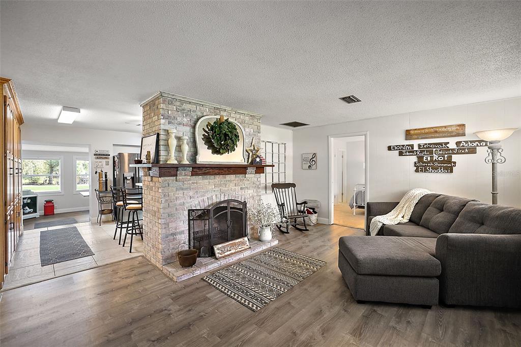 A living room features a central brick fireplace, wood-look flooring, and a gray sectional sofa — 10303 SE SUNSET HARBOR ROAD, SUMMERFIELD, FL