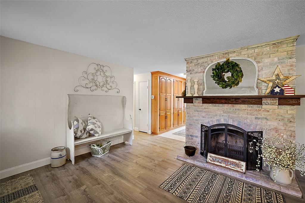 A living room features a brick fireplace, wood-look flooring, and a white wooden bench — 10303 SE SUNSET HARBOR ROAD, SUMMERFIELD, FL