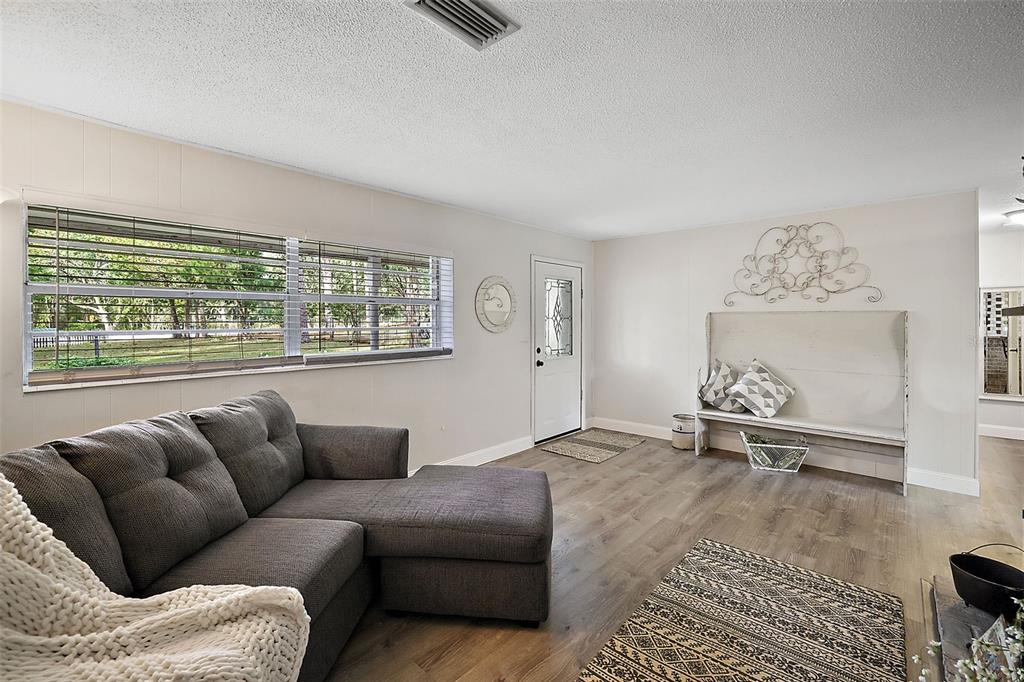 A living room with wood-look flooring, a gray sectional sofa, and a white entryway door — 10303 SE SUNSET HARBOR ROAD, SUMMERFIELD, FL