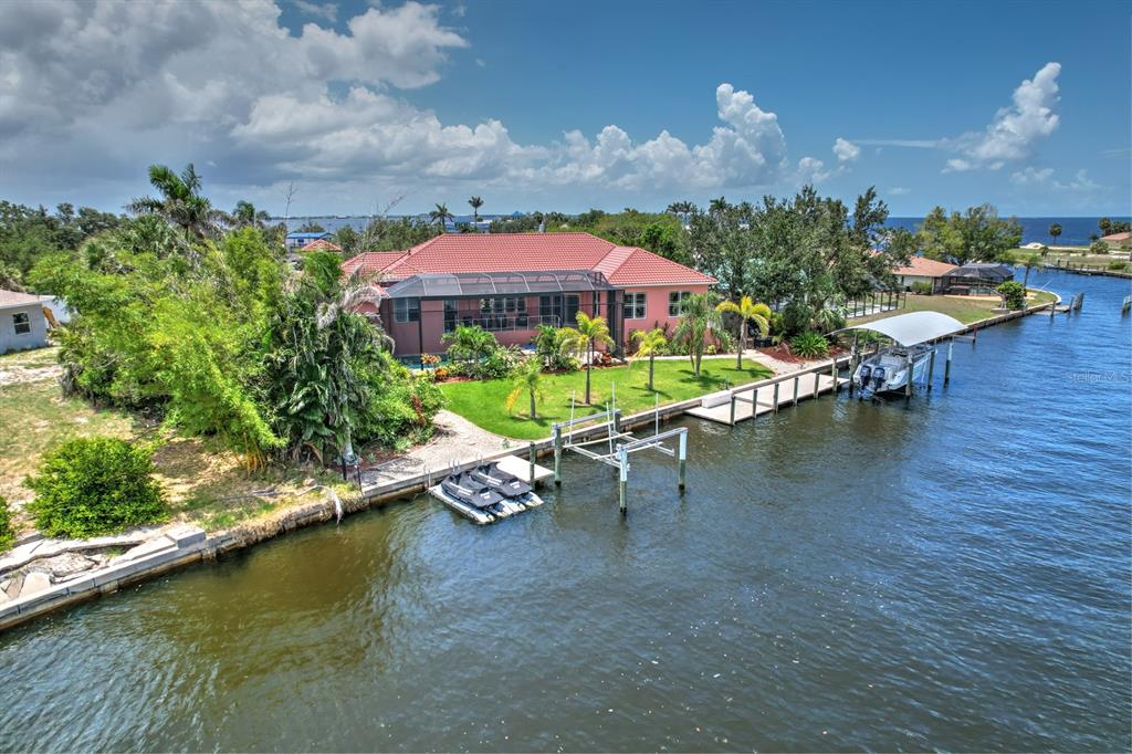An aerial view of a pink waterfront house with a boat lift and jet skis — 4409 CREWS COURT, PORT CHARLOTTE, FL