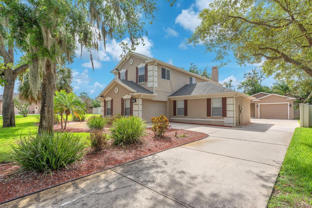 A two-story beige house with a concrete driveway, attached garage, and landscaped front yard — 8805 CROSS LANDING LANE, RIVERVIEW, FL