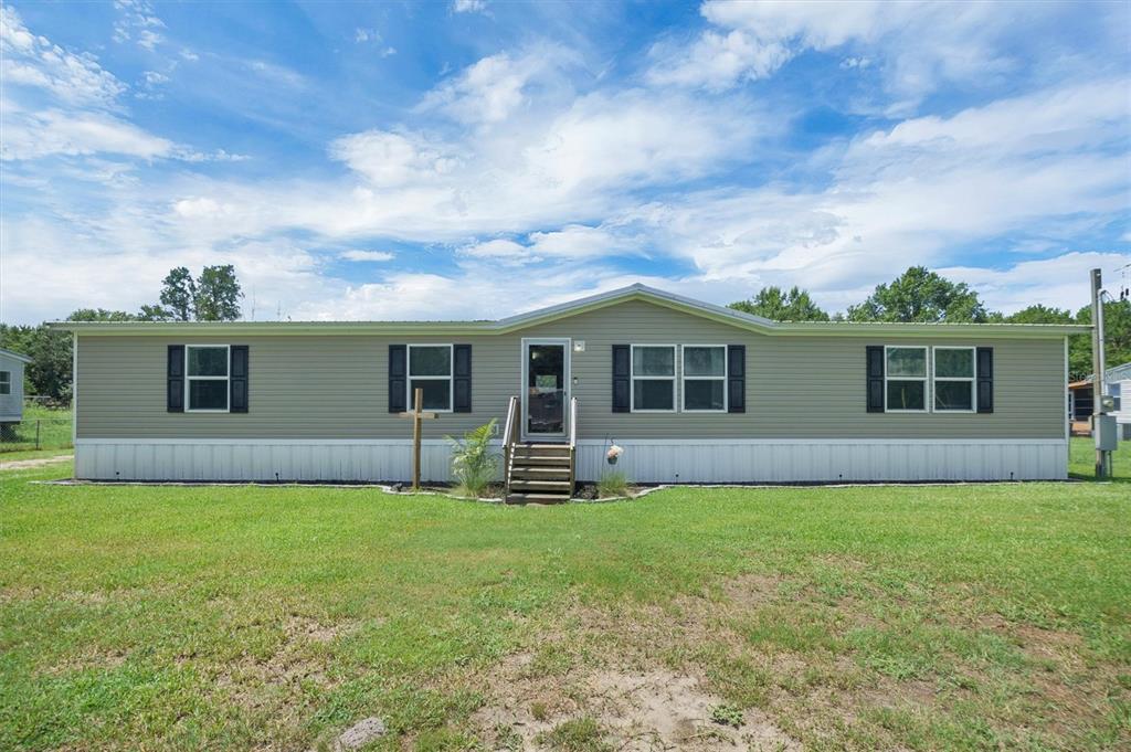 A single-story manufactured home with light-colored siding and black shutters sits on a grassy lot — 4237 COYOTE TRAIL, POLK CITY, FL