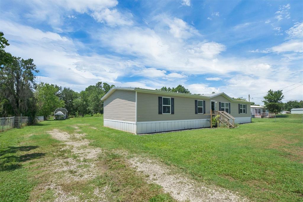 A tan manufactured home sits on a grassy lot with a gravel driveway and shed — 4237 COYOTE TRAIL, POLK CITY, FL