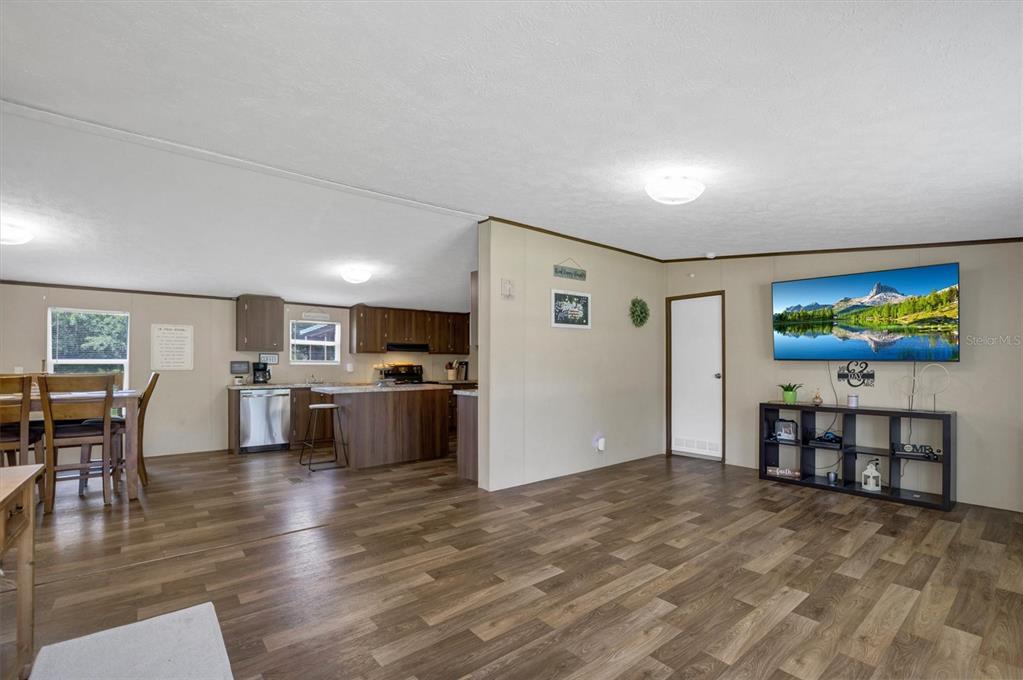 An open-concept living room and kitchen featuring wood-look flooring and a wall-mounted television — 4237 COYOTE TRAIL, POLK CITY, FL
