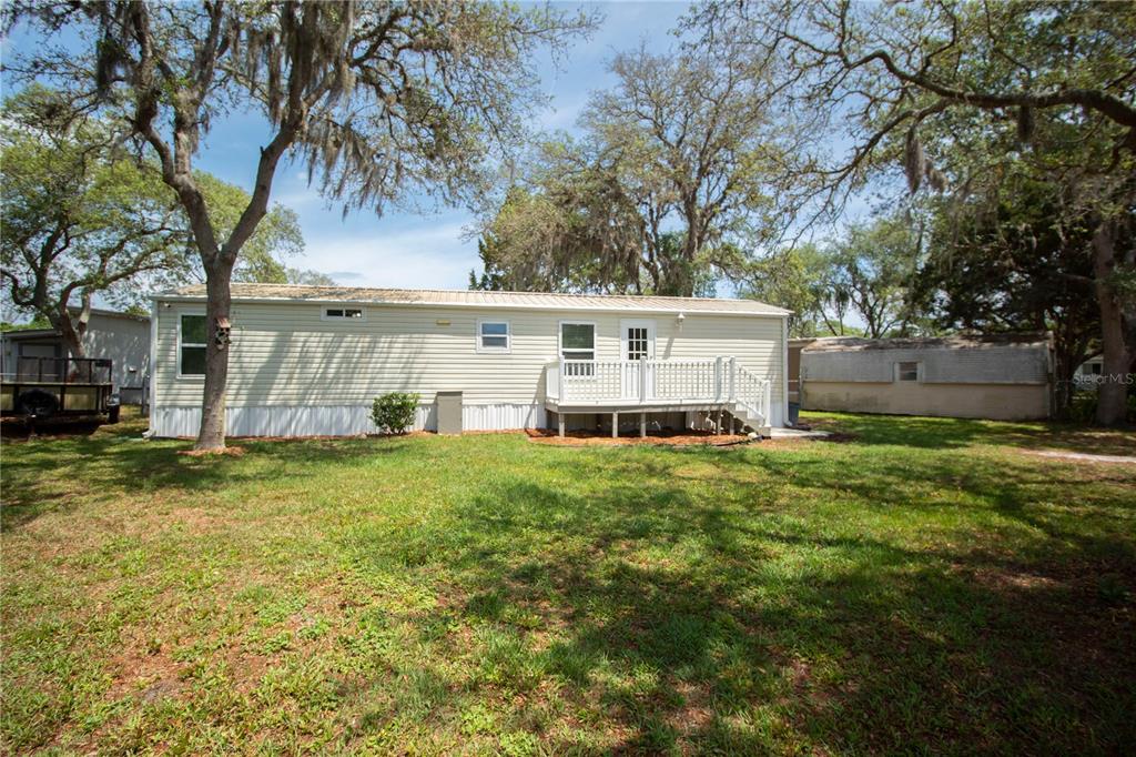 A single-story mobile home with light siding, a wooden deck, and surrounding trees — 28 SHADY LANE S, PALM COAST, FL