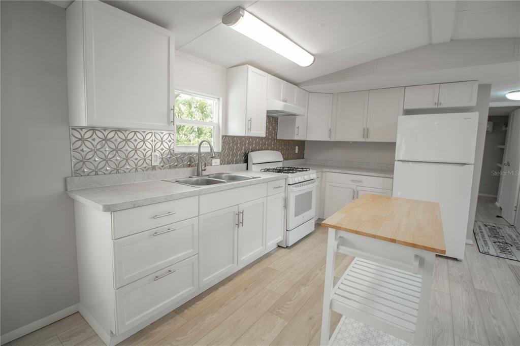 A kitchen with white cabinets, light wood-look flooring, a portable island, and a tiled backsplash — 28 SHADY LANE S, PALM COAST, FL