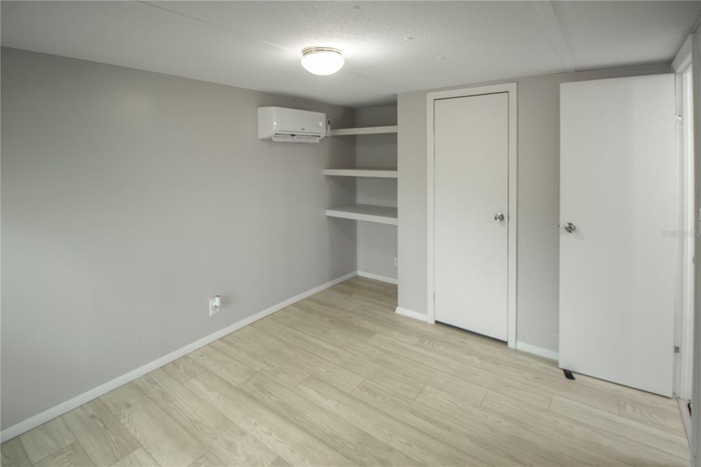 A room with light gray walls, wood-look flooring, built-in shelves, and a wall-mounted air conditioner — 28 SHADY LANE S, PALM COAST, FL