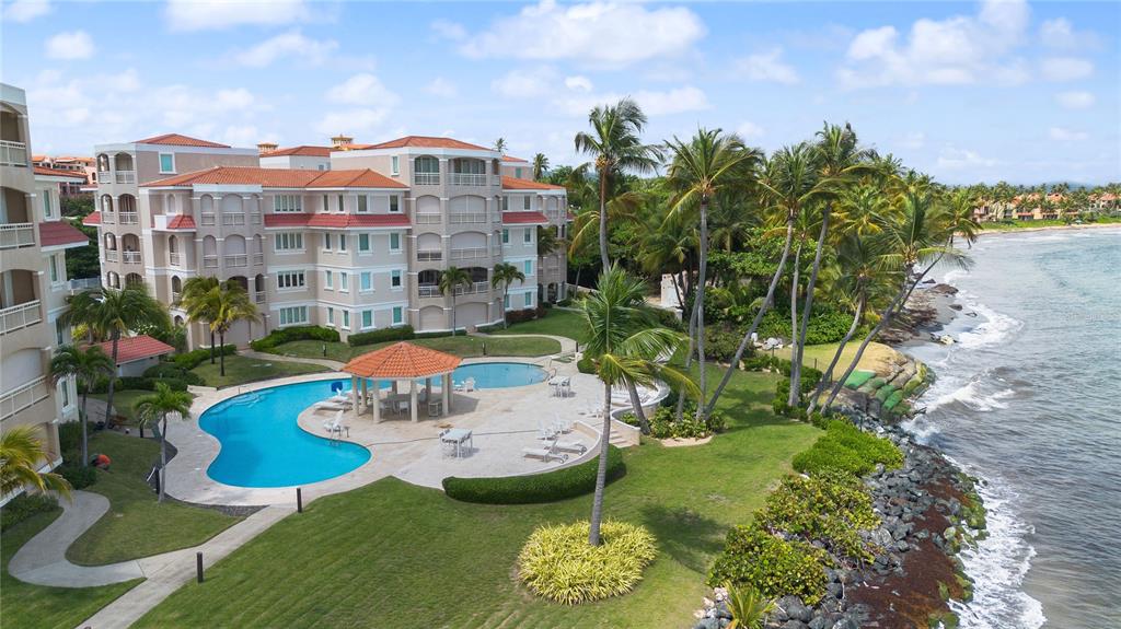 An aerial view shows a multi-story apartment building with a swimming pool and oceanfront lawn — Palmas del Mar PLAZA DEL MAR UNIT N-3A, HUMACAO, PR