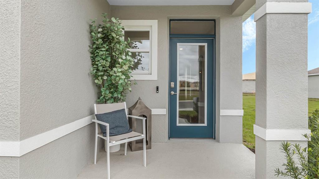 A covered porch features a blue glass-paneled door, a chair, and a potted plant — 3018 VICEROY COURT, POINCIANA, FL