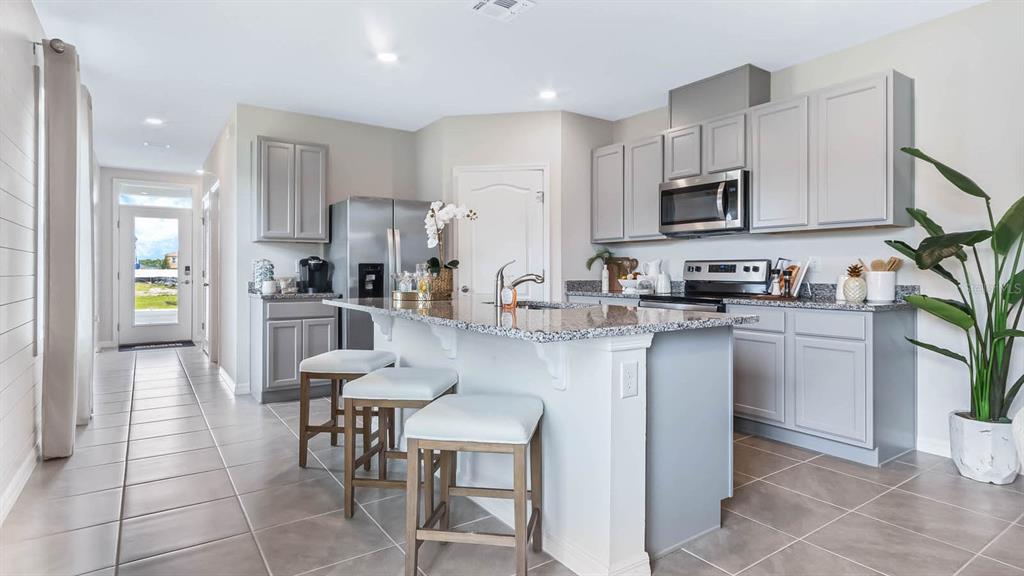 A kitchen features gray cabinets, granite countertops, a center island with stools, and tile flooring — 3018 VICEROY COURT, POINCIANA, FL