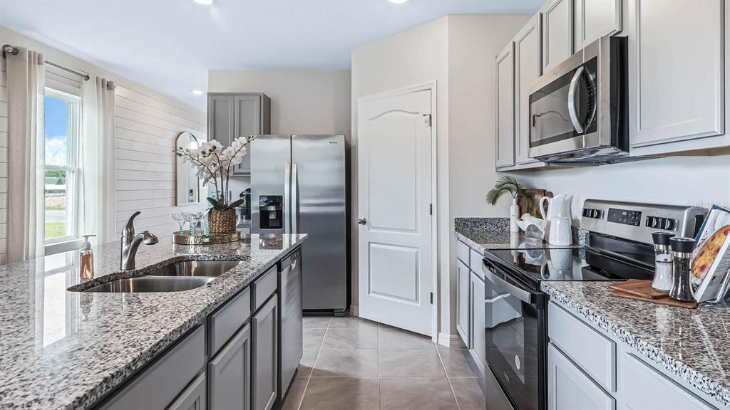 A kitchen features gray cabinets, granite countertops, stainless steel appliances, and a central island — 3018 VICEROY COURT, POINCIANA, FL