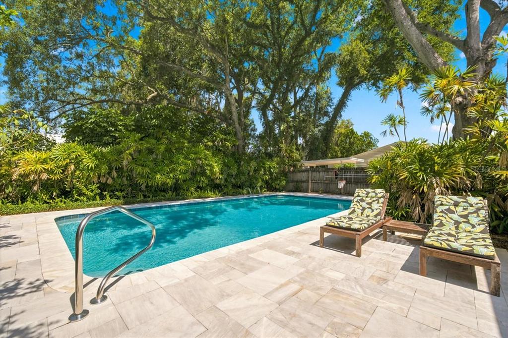A rectangular swimming pool with a stone patio and lounge chairs under large trees — 10502 SAGO ROAD, TAMPA, FL