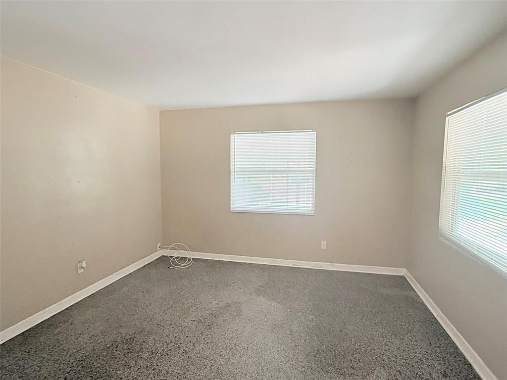 An empty bedroom features beige walls, gray carpeting, and two windows with white blinds — 1304 BROWNING STREET, CLEARWATER, FL