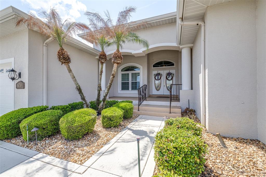 The exterior of a house features a paved walkway, manicured shrubs, and a covered entryway — 6758 HUNTINGTON HILLS BOULEVARD, LAKELAND, FL