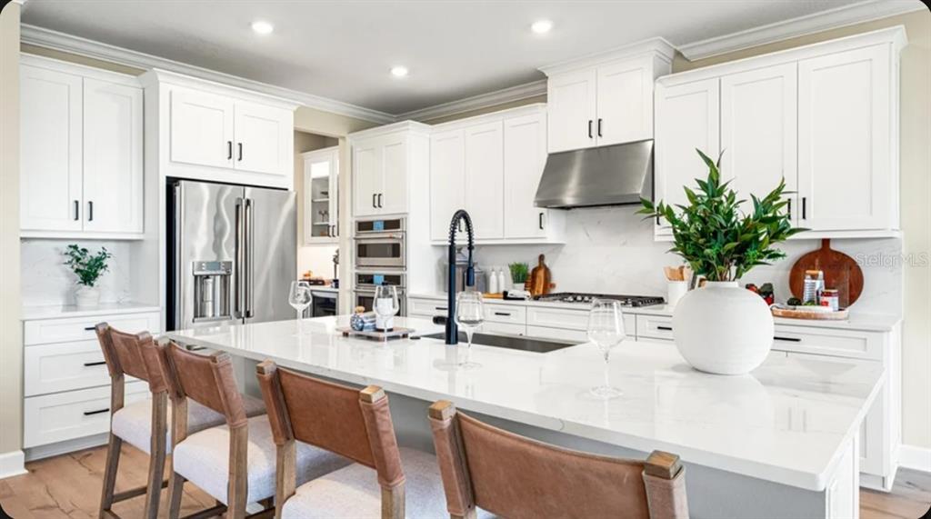 A modern white kitchen features a large quartz island, stainless steel appliances, and wood flooring — 12517 WHARF TERRACE, PALMETTO, FL