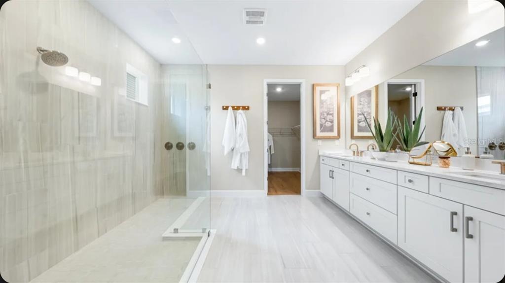 A modern bathroom features a glass-enclosed walk-in shower, white double vanity, and light tile flooring — 12517 WHARF TERRACE, PALMETTO, FL