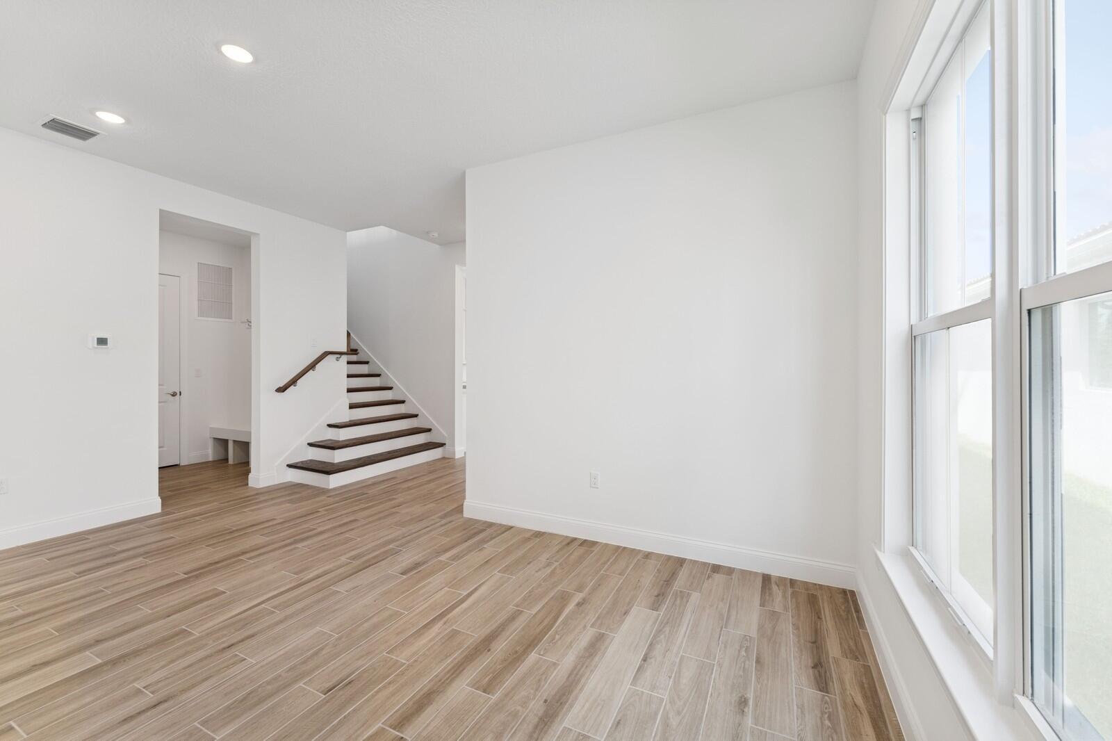 An interior view of a room with wood-look tile flooring, white walls, and a staircase — 6799 SE Lost Pine Drive, Stuart FL 34997, STUART, FL