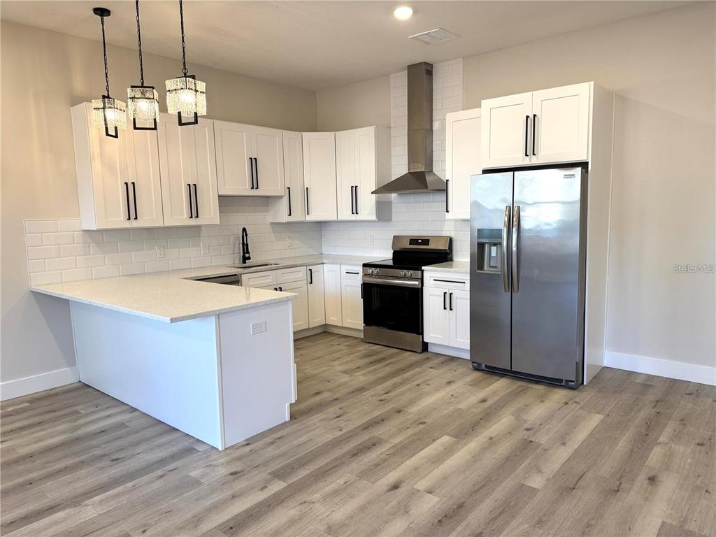 A kitchen features white cabinets, stainless steel appliances, a subway tile backsplash, and wood flooring — 1039 53RD AVENUE N, ST PETERSBURG, FL