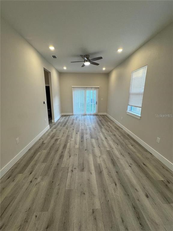 An empty living room features light wood-look flooring, recessed lighting, a ceiling fan, and sliding doors — 1039 53RD AVENUE N, ST PETERSBURG, FL