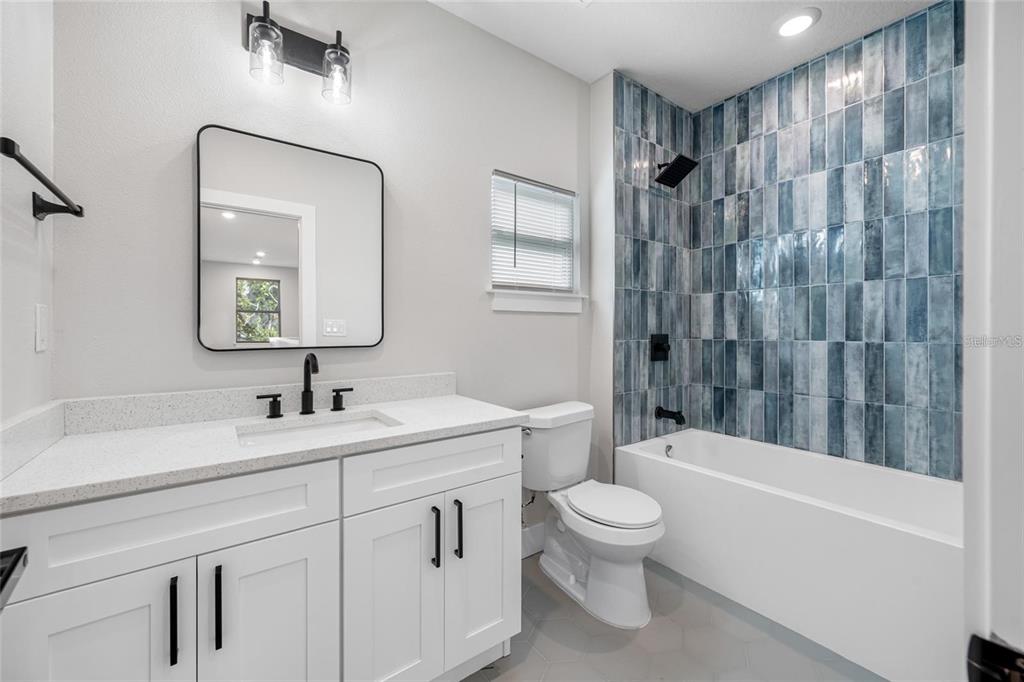 A bathroom features a white vanity, a black-framed mirror, and a blue-tiled bathtub shower — 1039 53RD AVENUE N, ST PETERSBURG, FL
