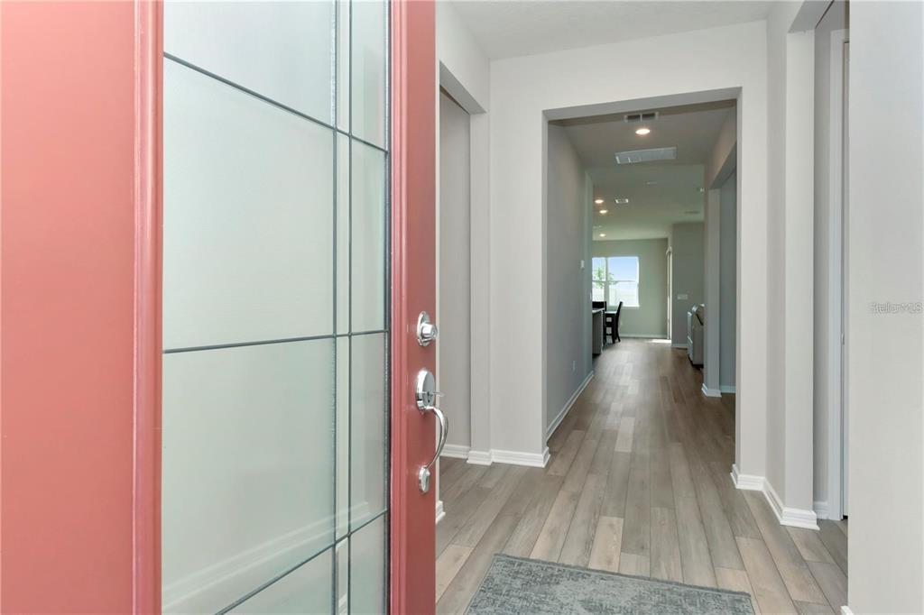 A view from an open red front door into a hallway with light wood flooring — 1991 SPRING SHOWER CIRCLE, KISSIMMEE, FL