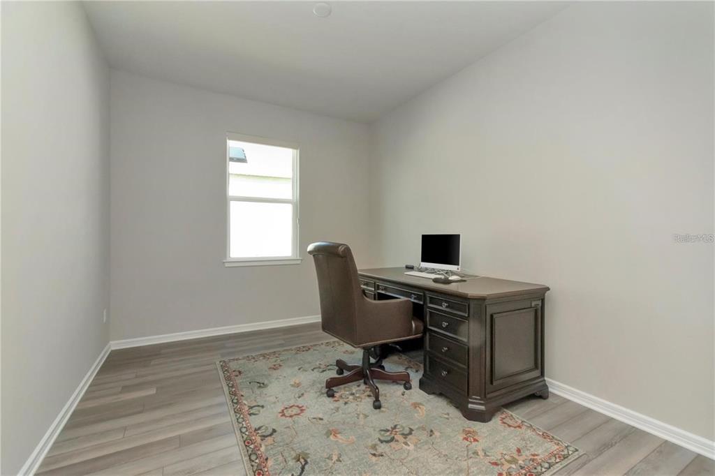 A home office features gray wood-look flooring, a brown desk, and a patterned area rug — 1991 SPRING SHOWER CIRCLE, KISSIMMEE, FL