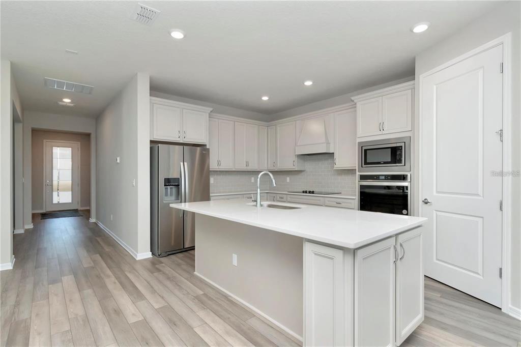 A modern kitchen features white cabinetry, stainless steel appliances, a center island, and wood flooring — 1991 SPRING SHOWER CIRCLE, KISSIMMEE, FL