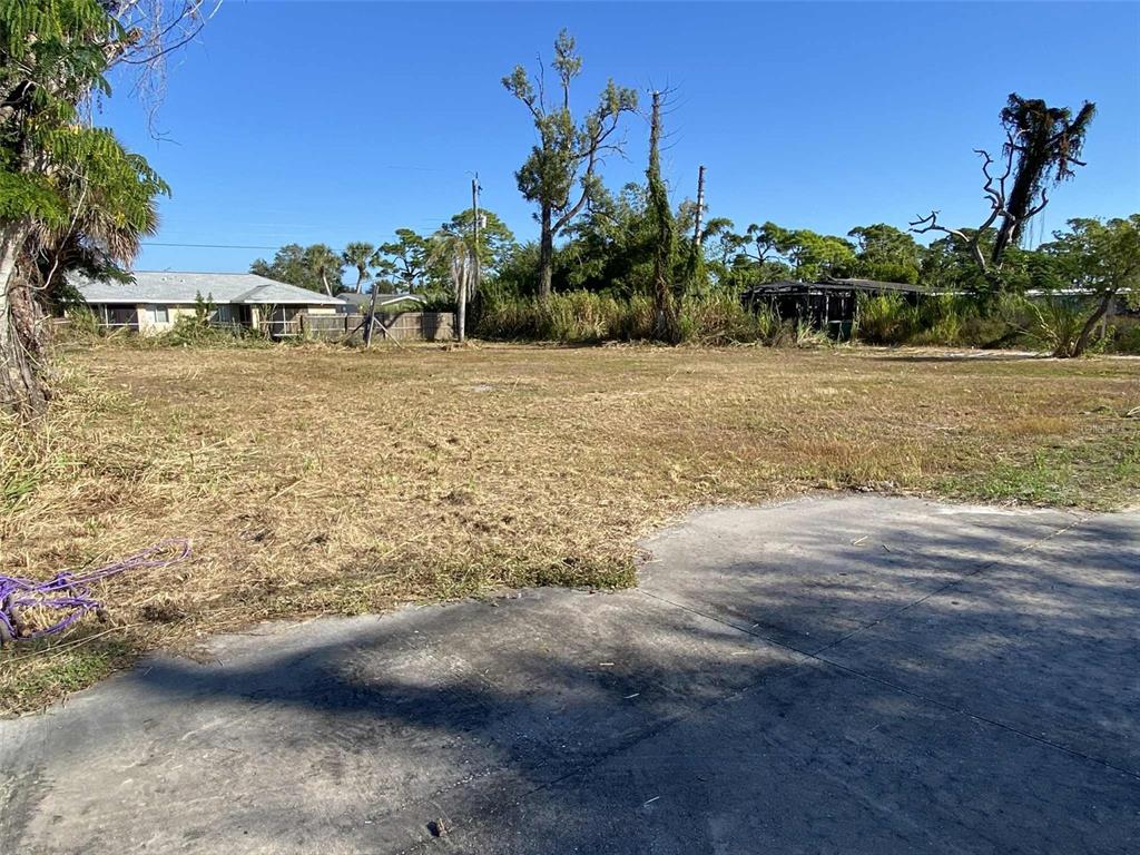 A vacant, grassy lot with a concrete driveway in the foreground and surrounding trees — 7439 SAN CASA DRIVE, ENGLEWOOD, FL