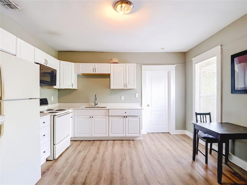 A kitchen features white cabinets, light wood-look flooring, a white stove, and a dining table — 2020 DAVIS STREET, TAMPA, FL