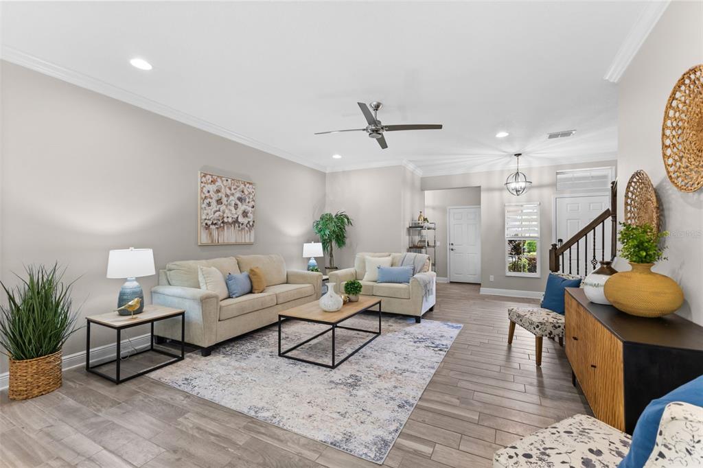 A living room features light-colored sofas, a patterned area rug, and wood-look tile flooring — 11458 CROWNED SPARROW LANE, TAMPA, FL