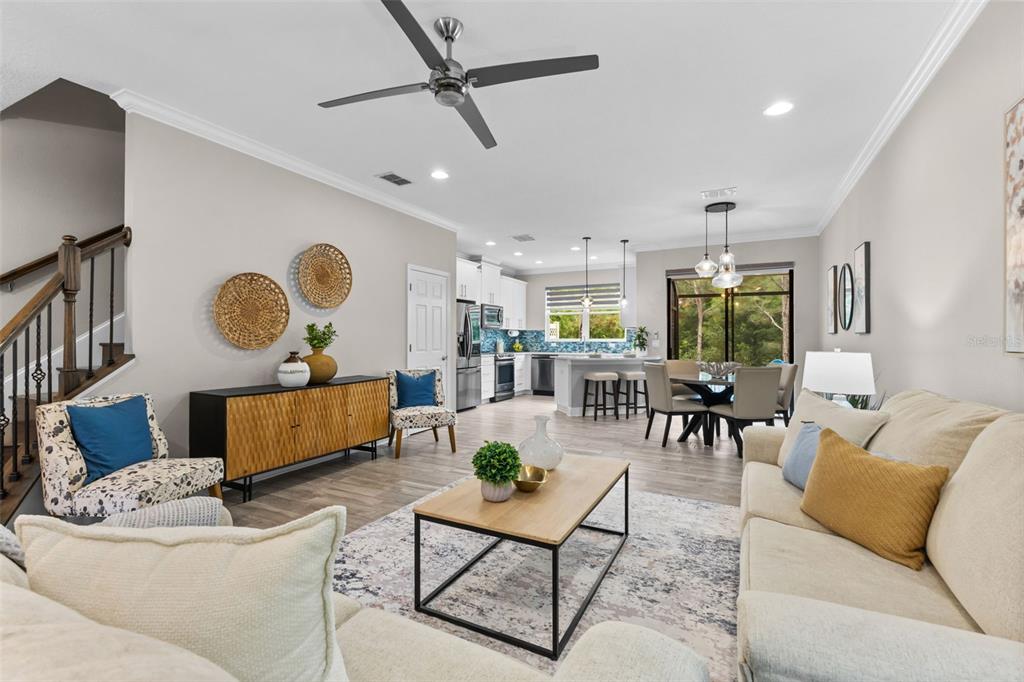 An open-concept living room and kitchen featuring light wood floors, a ceiling fan, and furniture — 11458 CROWNED SPARROW LANE, TAMPA, FL