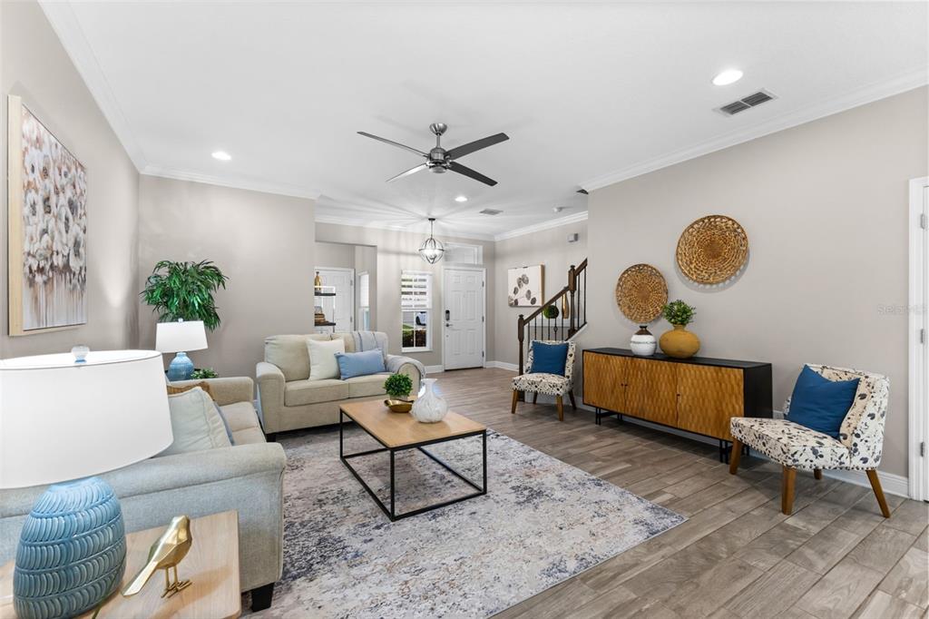 A living room features light gray walls, wood-look tile flooring, a ceiling fan, and neutral furniture — 11458 CROWNED SPARROW LANE, TAMPA, FL