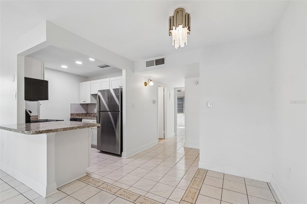 A kitchen with white cabinets, granite countertops, and stainless steel appliances opens to a dining area — 237 S MCMULLEN BOOTH ROAD UNIT 51, CLEARWATER, FL