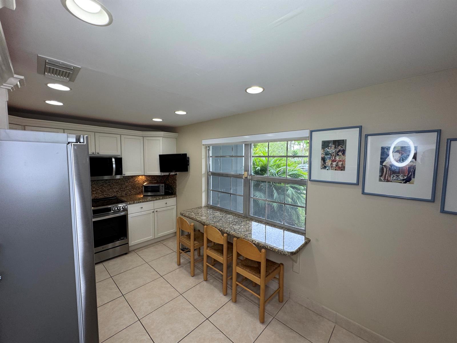 A kitchen features white cabinets, granite countertops, a breakfast bar with three chairs, and tile flooring — 625 Oaks Drive # 106, Pompano Beach FL 33069, POMPANO BEACH, FL