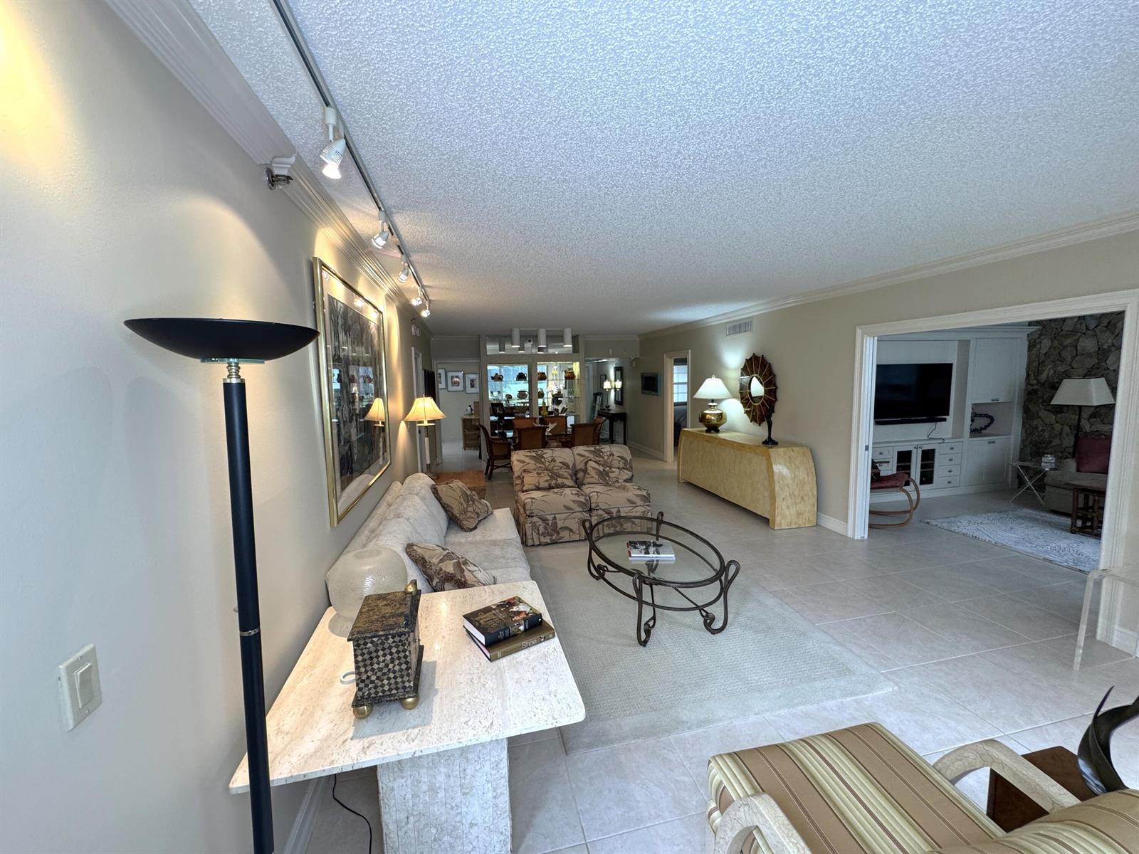 A living room features a beige sofa, glass coffee table, and track lighting on the ceiling — 625 Oaks Drive # 106, Pompano Beach FL 33069, POMPANO BEACH, FL
