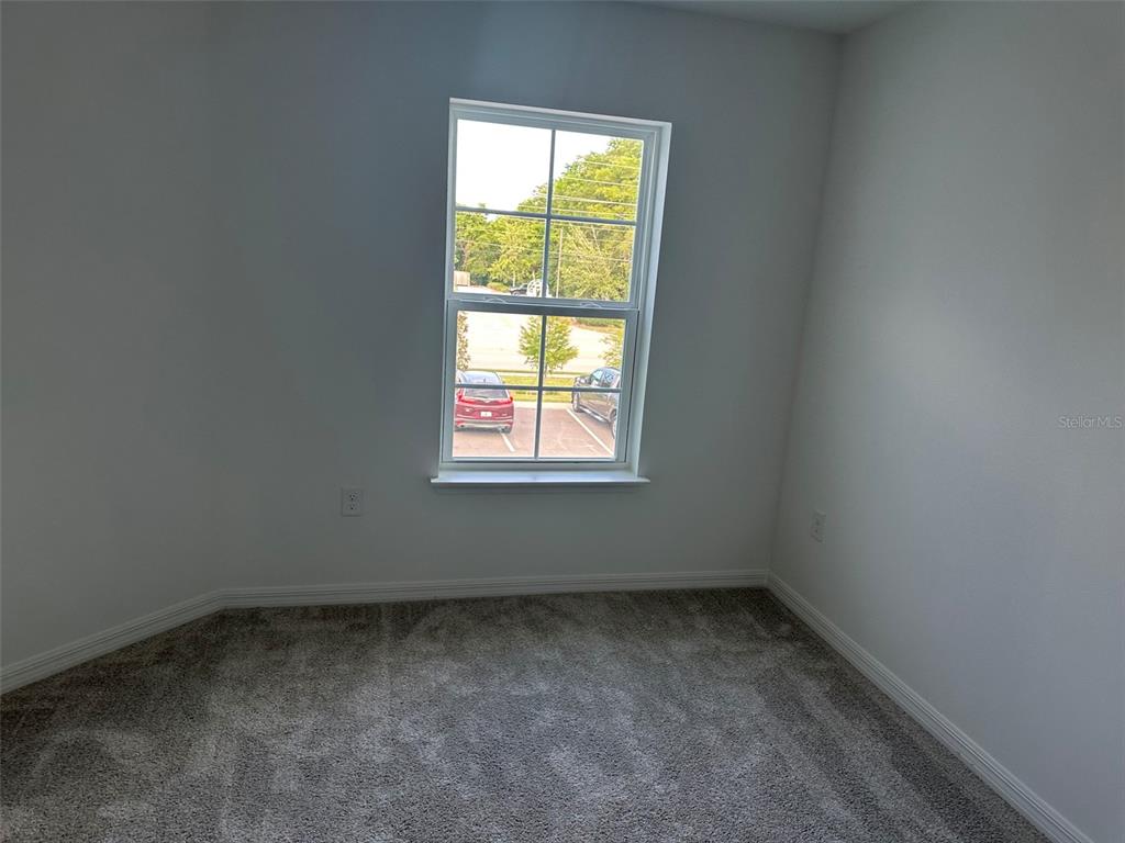 An empty bedroom features gray carpet, white walls, and a window overlooking a parking lot — 737 MAPLE OAK DRIVE, DELAND, FL