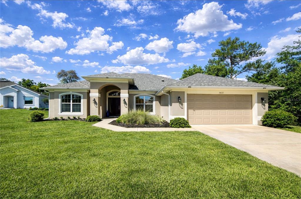 A single-story suburban house with a tan stucco exterior, a two-car garage, and a lawn — 9832 SW 46TH COURT, OCALA, FL