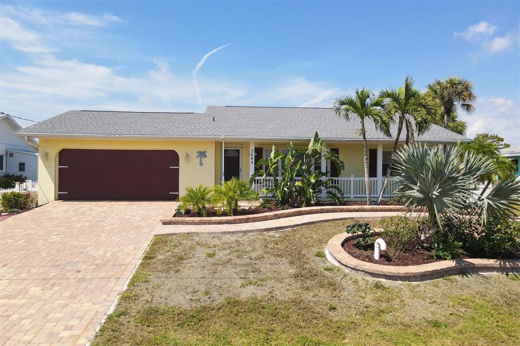 A single-story yellow house with a two-car garage, paved driveway, and landscaped front yard — 2684 TITANIA ROAD, ENGLEWOOD, FL