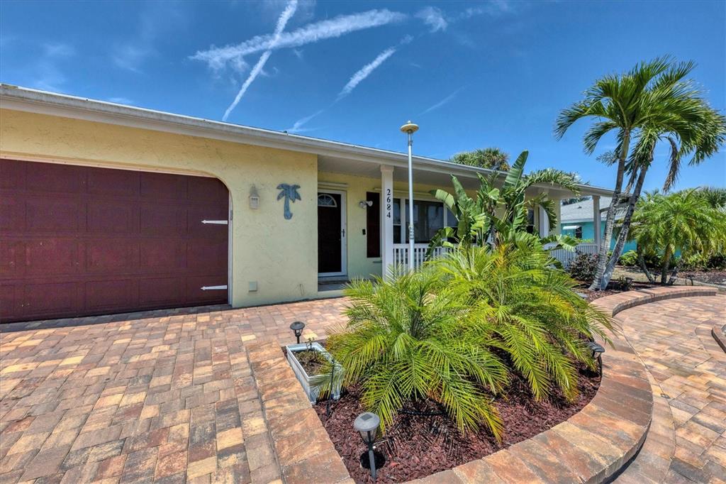 A yellow house exterior features a brown garage door, a paved driveway, and palm trees — 2684 TITANIA ROAD, ENGLEWOOD, FL