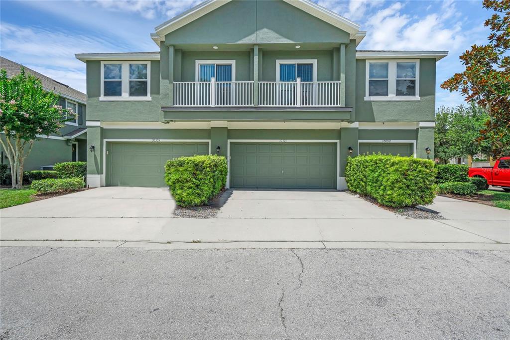 The exterior of a two-story green townhouse features three garage doors and a shared balcony — 10802 ECLIPSE LILY WAY UNIT 50A, ORLANDO, FL
